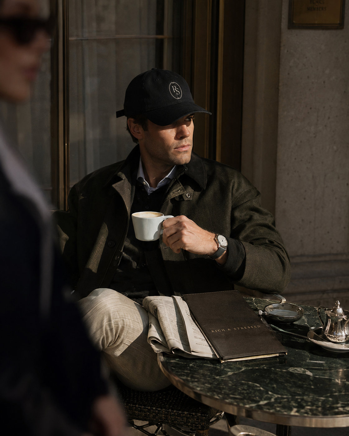 Man in the Rich and Stressed cap with an espresso at a marble café table